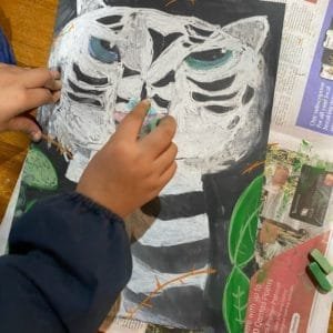 A young artist's hands are seen working on the white tiger pastel artwork, adding details with a pastel stick.